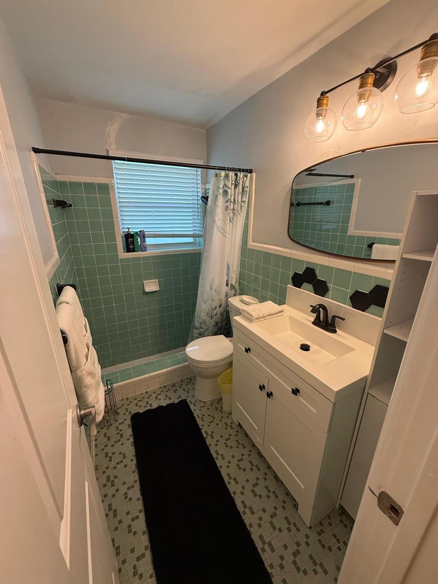 A bathroom features green square wall tiles, a white vanity, and a shower curtain — 27 NW 14th Avenue, Delray Beach FL 33444, DELRAY BEACH, FL