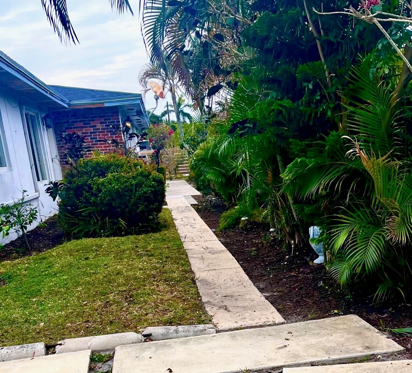 A concrete walkway leads past a brick-accented house and lush tropical landscaping in a yard — 27 NW 14th Avenue, Delray Beach FL 33444, DELRAY BEACH, FL