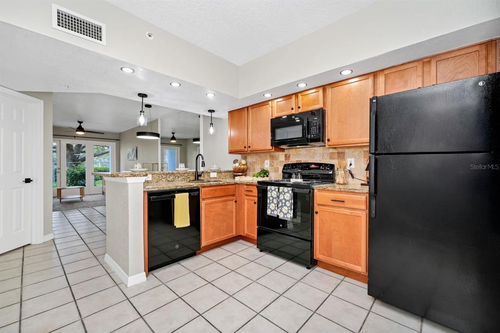 A kitchen with light wood cabinets, black appliances, granite countertops, and light-colored tile flooring — 2954 SADINA STREET UNIT 103, KISSIMMEE, FL