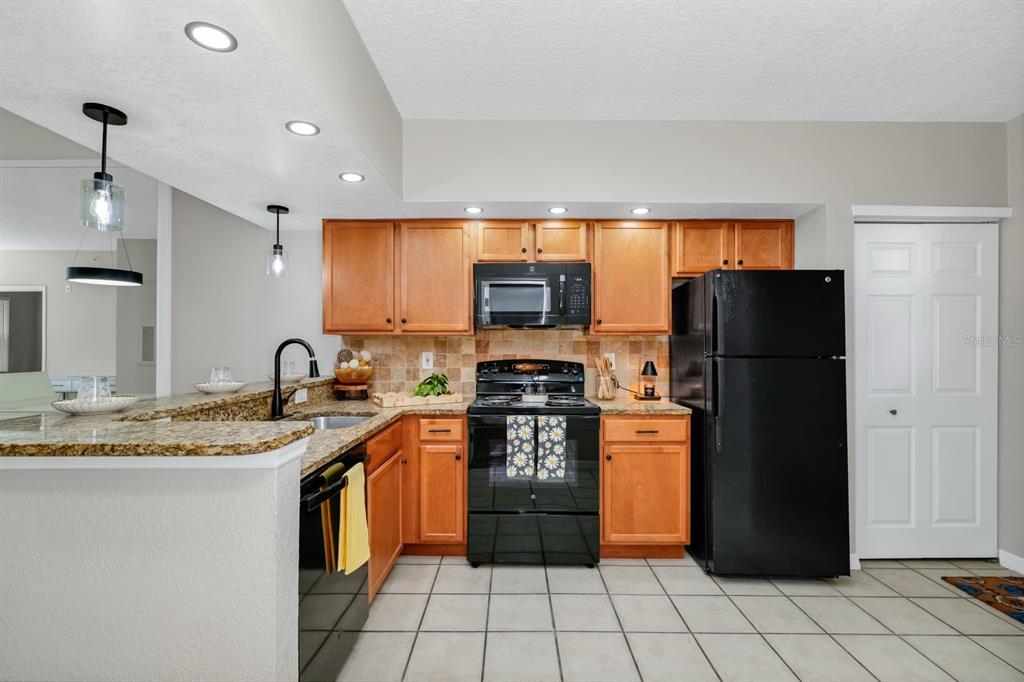 A kitchen features wood cabinets, granite countertops, black appliances, and a tiled floor — 2954 SADINA STREET UNIT 103, KISSIMMEE, FL