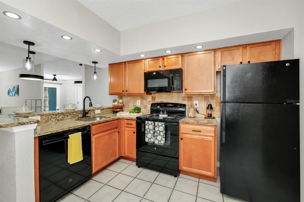 A kitchen with wood cabinets, black appliances, granite countertops, and light-colored tile flooring — 2954 SADINA STREET UNIT 103, KISSIMMEE, FL