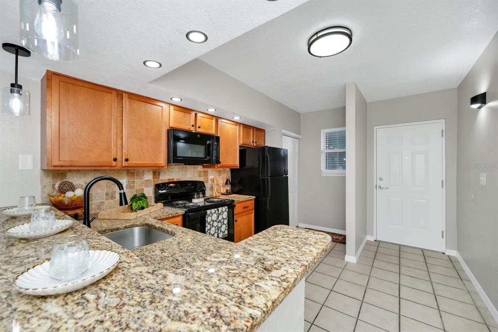 A kitchen features wood cabinets, granite countertops, a black microwave, and a tiled floor — 2954 SADINA STREET UNIT 103, KISSIMMEE, FL
