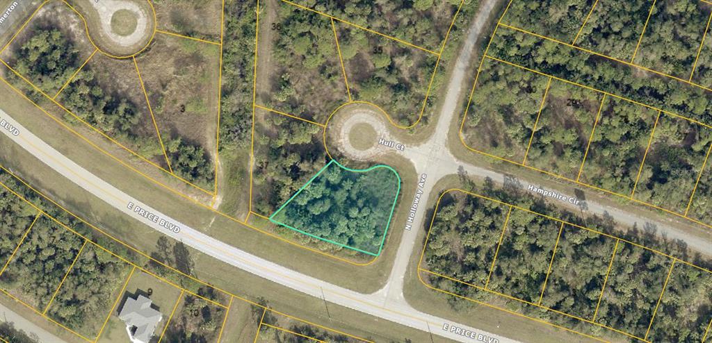 An aerial view shows a vacant, wooded corner lot outlined in teal near a road intersection — N HOLLOWAY AVENUE, NORTH PORT, FL