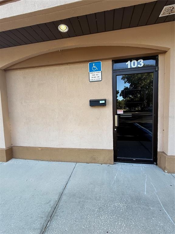 An exterior view of a commercial building entrance with a glass door labeled 103 — 2011 SW 20TH PLACE UNIT 103, OCALA, FL