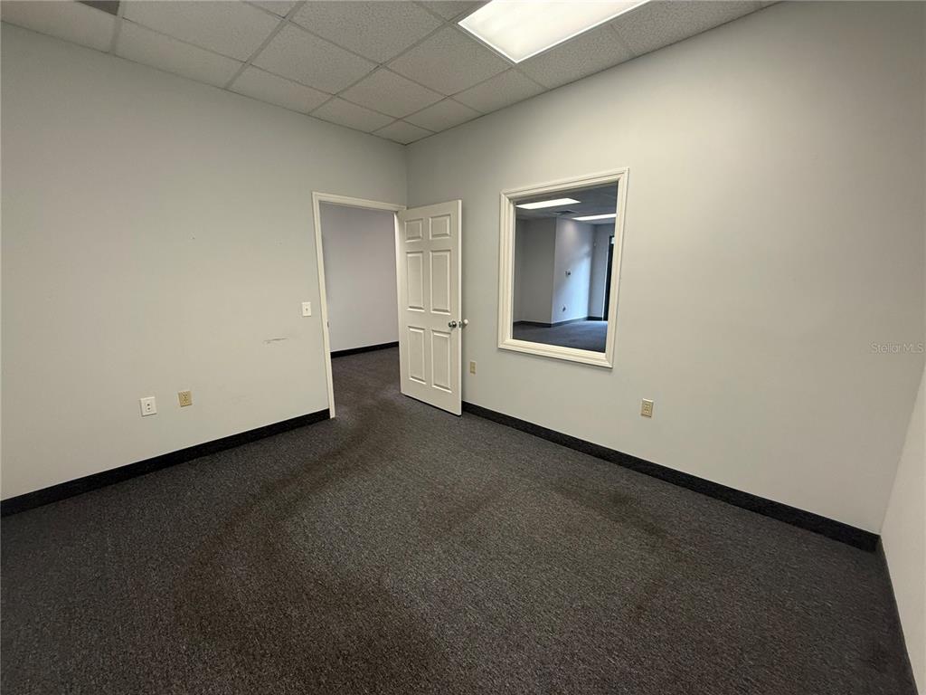 An empty office with gray carpet, light walls, a white door, and an interior window — 2011 SW 20TH PLACE UNIT 103, OCALA, FL