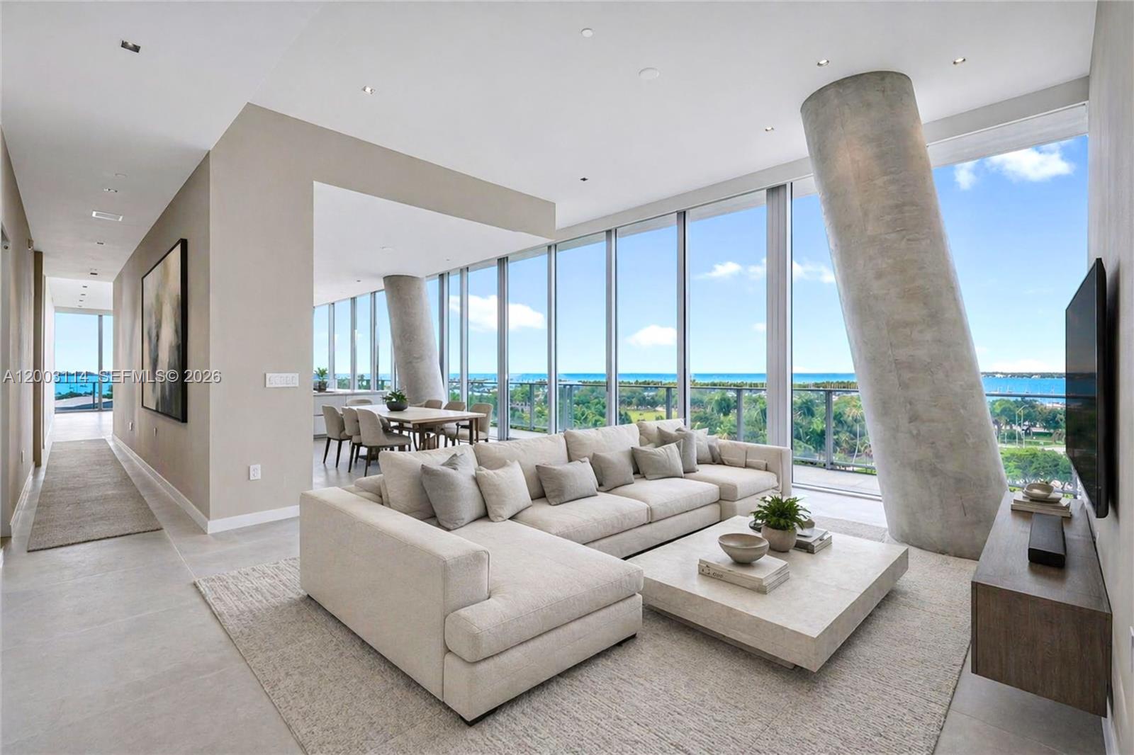 A modern living room features a large sectional sofa, concrete columns, and floor-to-ceiling windows — 2675 S Bayshore Dr # 602S, Miami FL 33133, MIAMI, FL