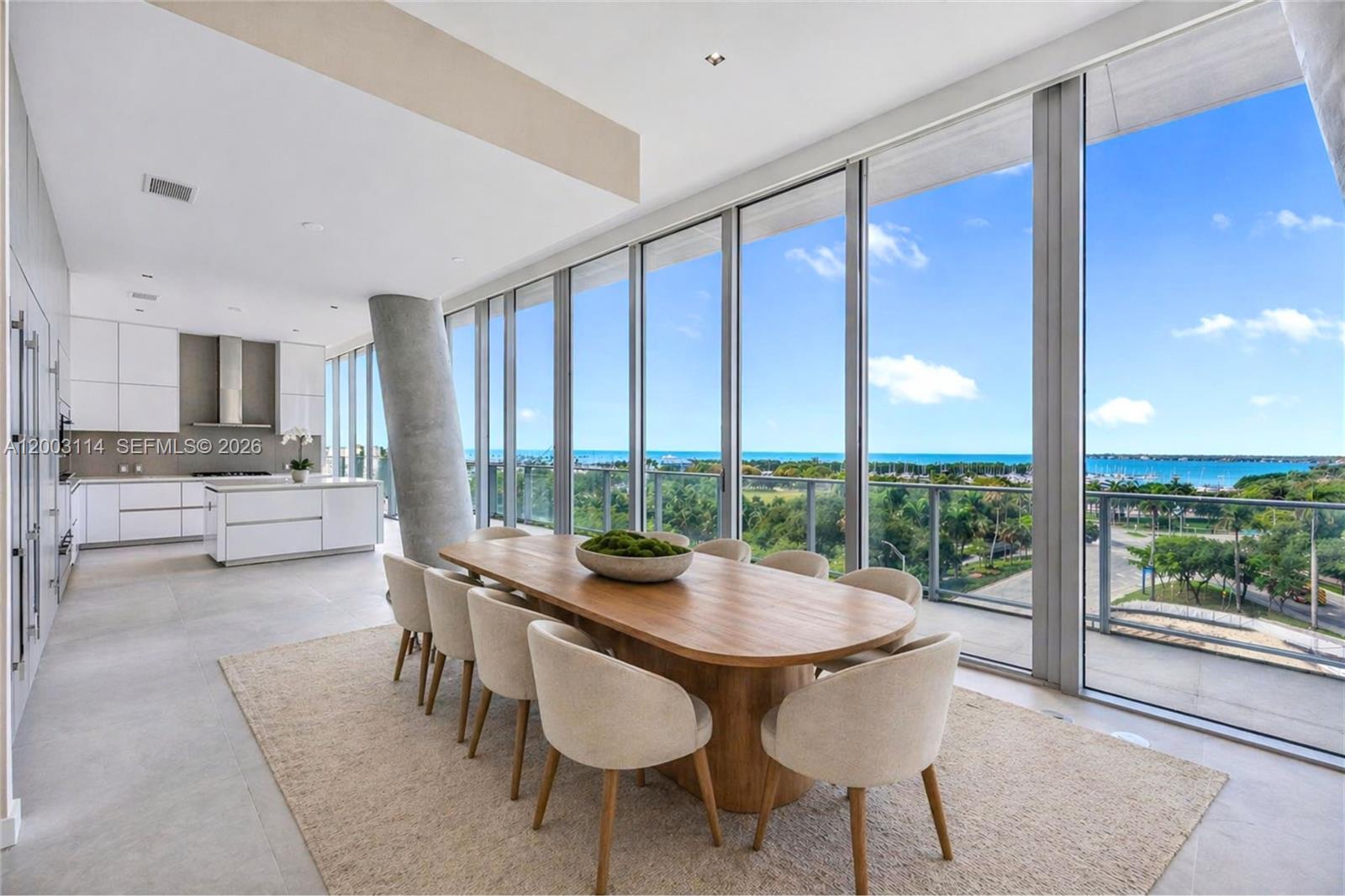A modern dining area features a wooden table, upholstered chairs, and floor-to-ceiling windows overlooking water — 2675 S Bayshore Dr # 602S, Miami FL 33133, MIAMI, FL