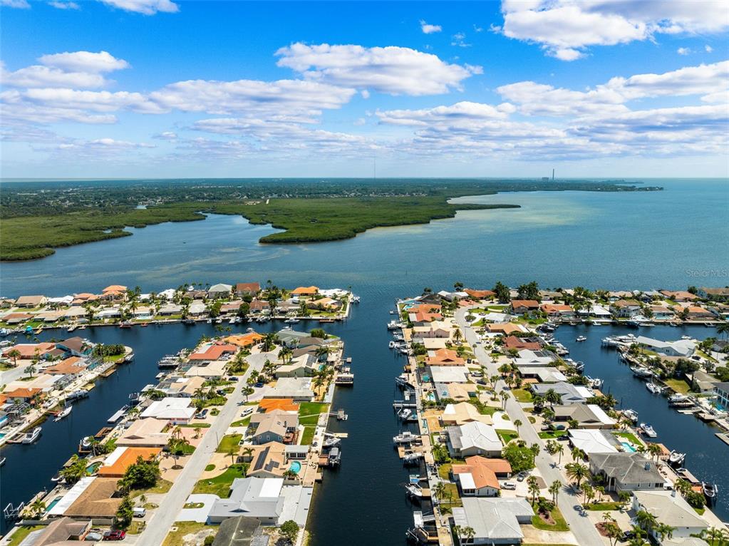 A paved patio overlooks a canal with boat docks and residential homes in the background — 5041 CABRILLA COURT, NEW PORT RICHEY, FL