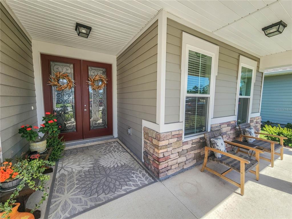 A covered front porch features a double door entry, stone siding, and two outdoor chairs — 158 WOOD STORK LANE, PALM COAST, FL