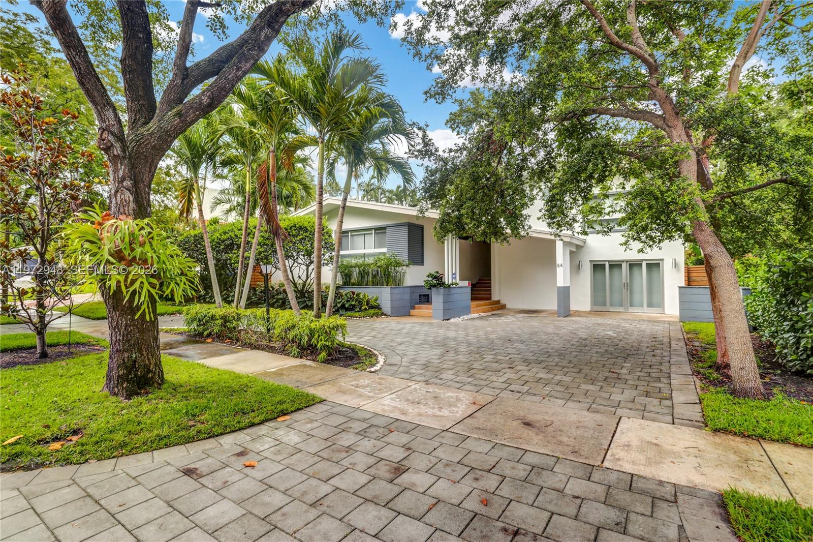 A modern two-story house with a paved driveway, palm trees, and lush landscaping — 84 Bay Heights Dr, Miami FL 33133, MIAMI, FL