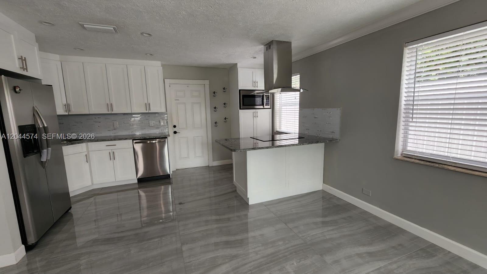 A kitchen features white cabinets, stainless steel appliances, a granite island, and gray tile flooring — LAKE WORTH, FL
