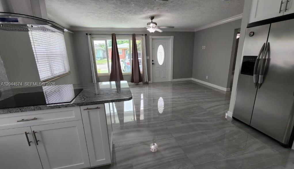 A kitchen with white cabinets, granite countertops, and gray tile flooring opens to an entryway — LAKE WORTH, FL