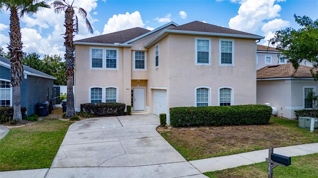 A two-story, light-colored stucco house with a concrete driveway and a small front lawn — 746 LOCKBREEZE DRIVE, DAVENPORT, FL
