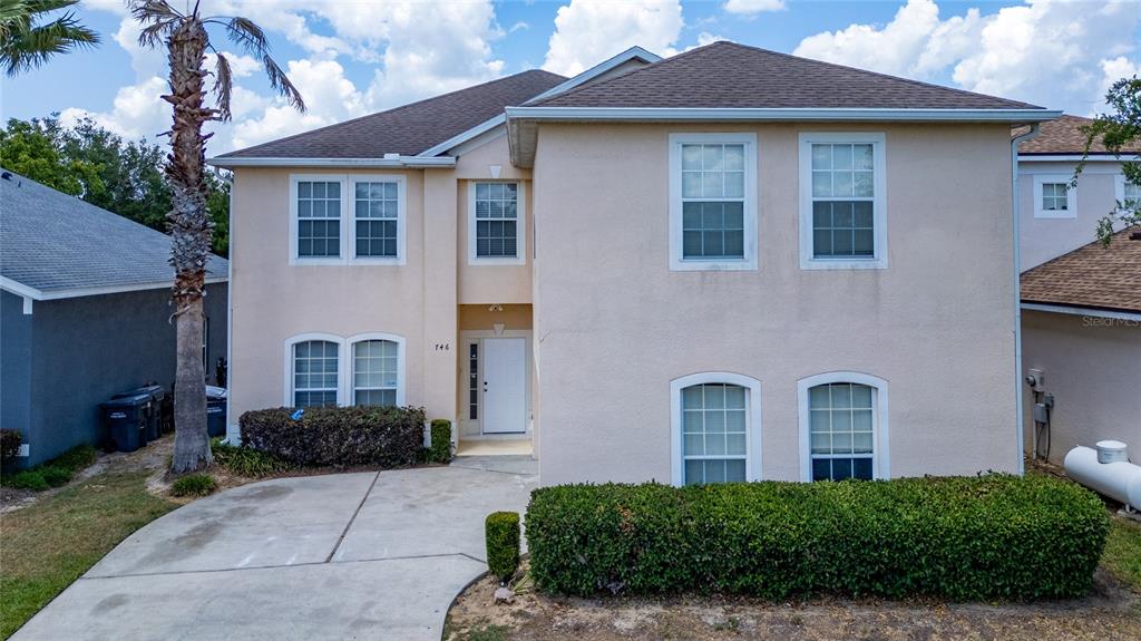 A two-story house with a beige stucco exterior, a concrete driveway, and a front hedge — 746 LOCKBREEZE DRIVE, DAVENPORT, FL