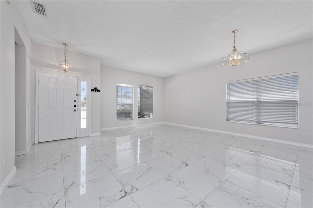 An empty room with white marble-look tile flooring, white walls, and two hanging light fixtures — 746 LOCKBREEZE DRIVE, DAVENPORT, FL