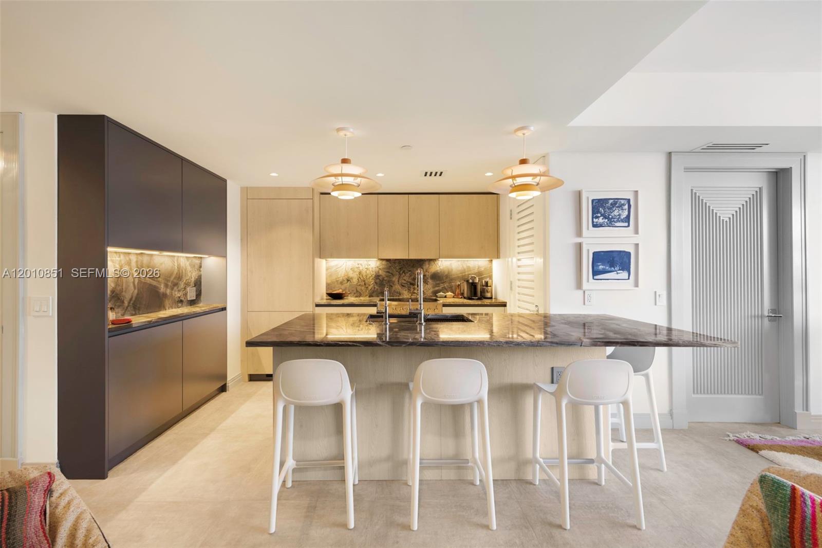 A modern kitchen features a dark marble island, light wood cabinetry, and three white stools — 5875 Collins Ave # 503, Miami Beach FL 33140, MIAMI BEACH, FL