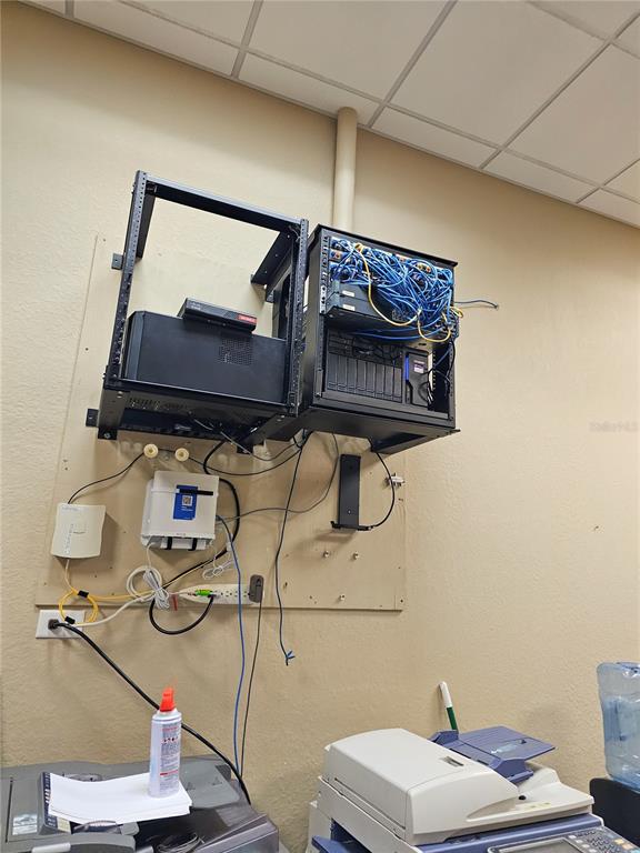 A wall-mounted network rack with cabling and equipment is installed above office printers — 422 S ALAFAYA TRAIL UNIT 30, ORLANDO, FL