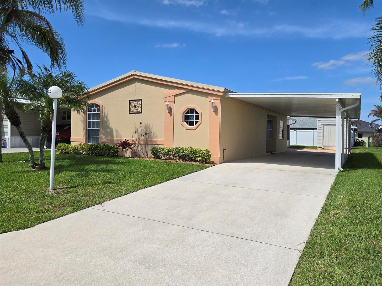 A single-story tan house with a concrete driveway, carport, and palm trees on a lawn — 4311 SW 9th Way, Okeechobee FL 34974, OKEECHOBEE, FL