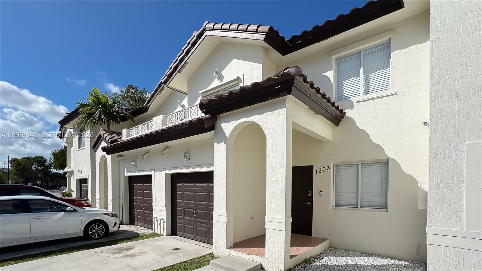 A two-story townhouse exterior features white stucco walls, brown garage doors, and tiled roofing — 8902 NW 109th Ct # 1203, Doral FL 33178, DORAL, FL