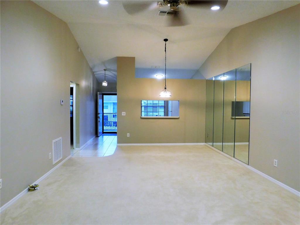 A living room with beige carpet, vaulted ceilings, mirrored walls, and a pass-through window — 2150 ELM STREET UNIT 606, DUNEDIN, FL
