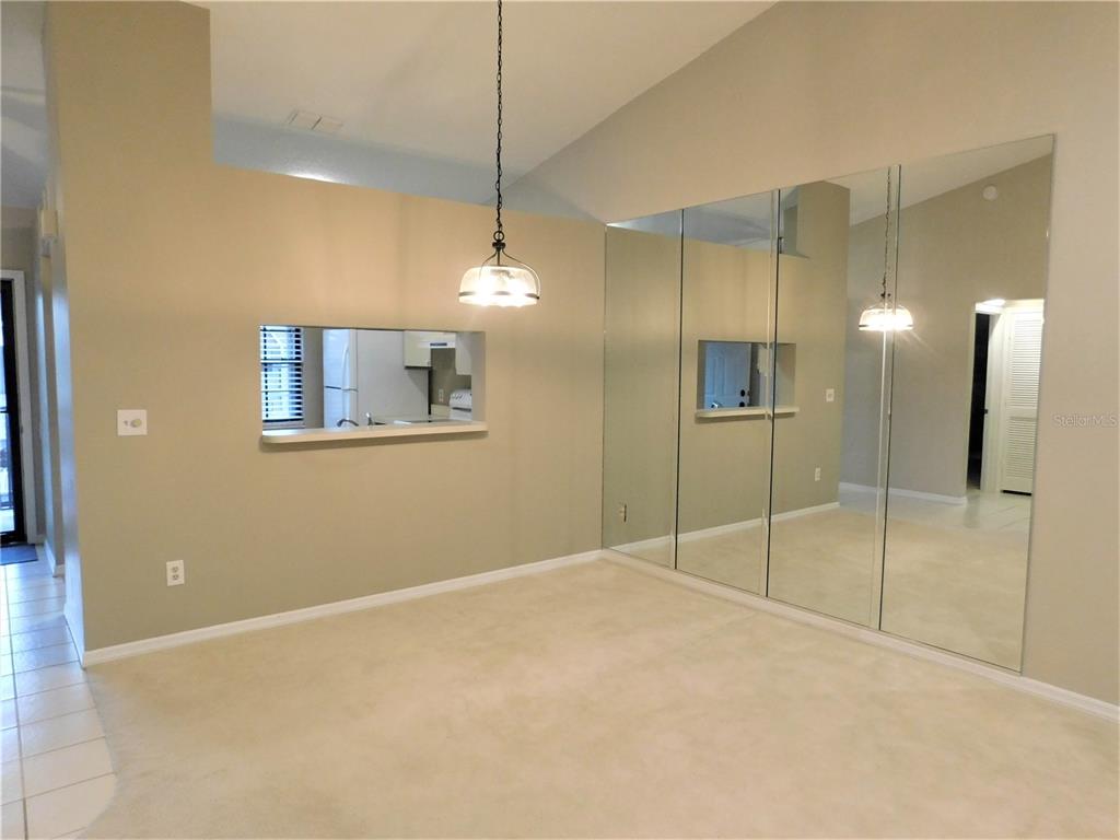 A dining area features beige carpeting, a pass-through window to the kitchen, and mirrored walls — 2150 ELM STREET UNIT 606, DUNEDIN, FL