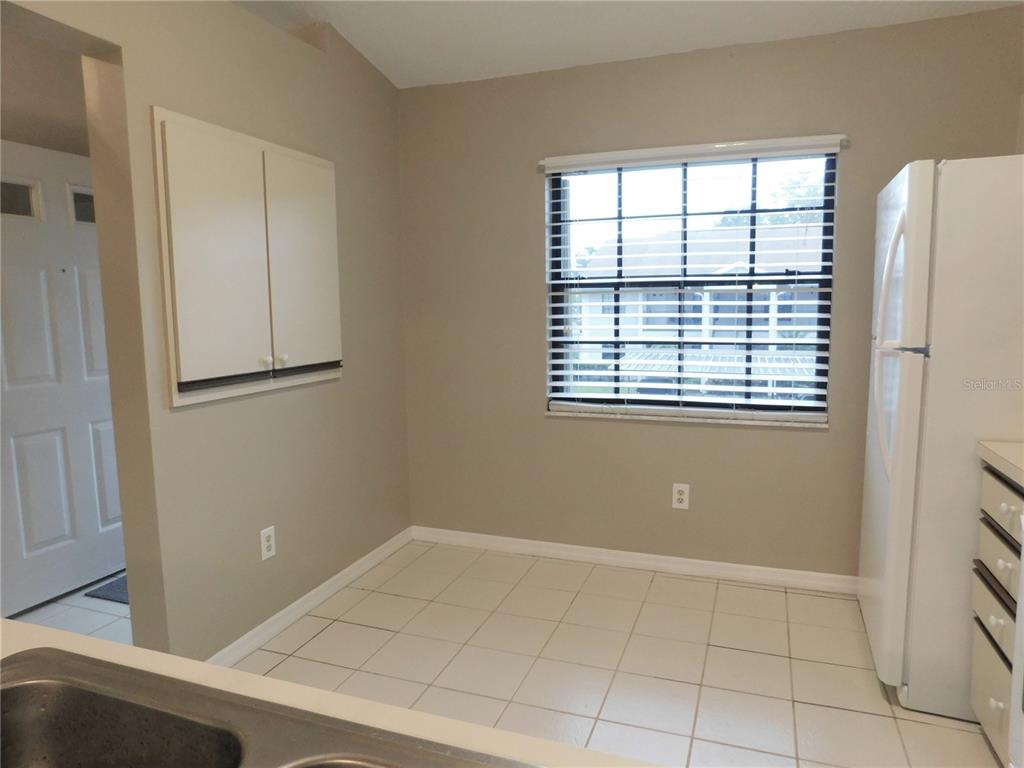 A kitchen features white tile flooring, beige walls, a window with blinds, and a refrigerator — 2150 ELM STREET UNIT 606, DUNEDIN, FL