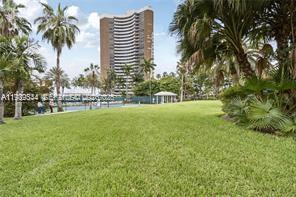 A grassy lawn leads toward a tall, curved residential building surrounded by palm trees — 770 NE 69th St # 6E, Miami FL 33138, MIAMI, FL