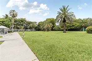 A paved walkway leads past a grassy lawn with several palm trees under a blue sky — 770 NE 69th St # 6E, Miami FL 33138, MIAMI, FL