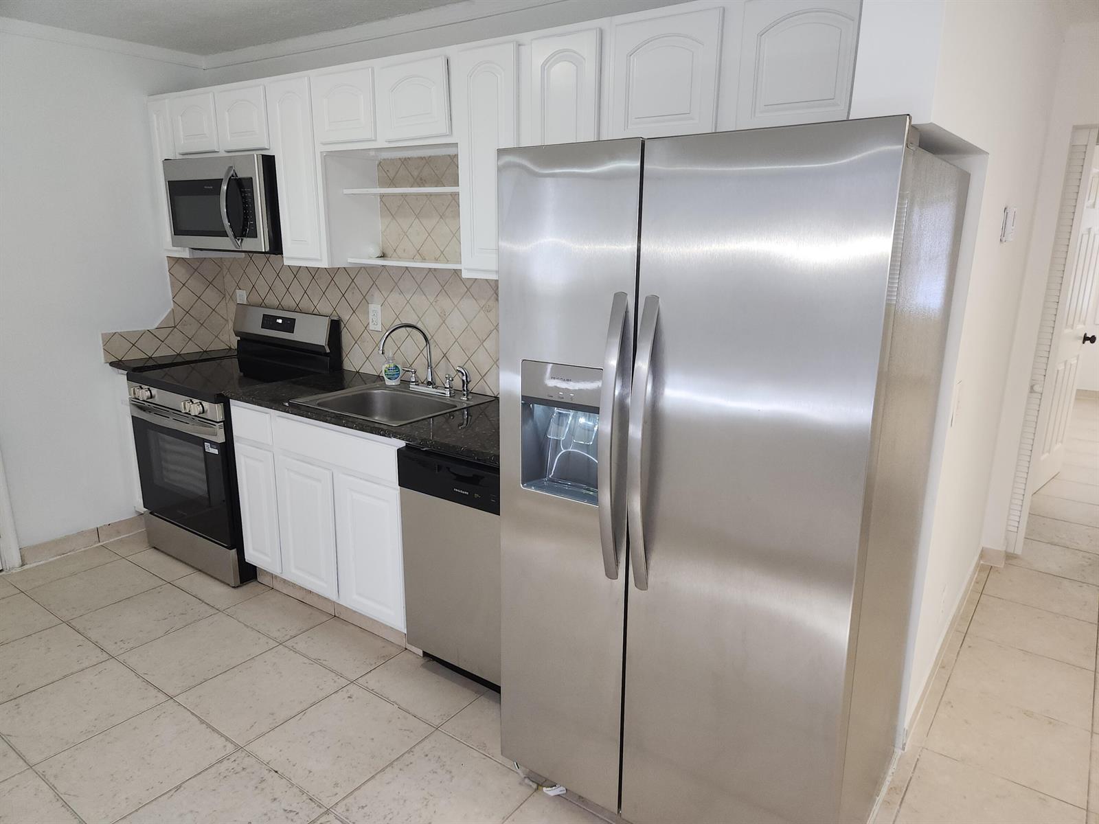 A kitchen featuring white cabinets, stainless steel appliances, dark countertops, and a tiled backsplash — 210 NW 13th Avenue, Delray Beach FL 33444, DELRAY BEACH, FL