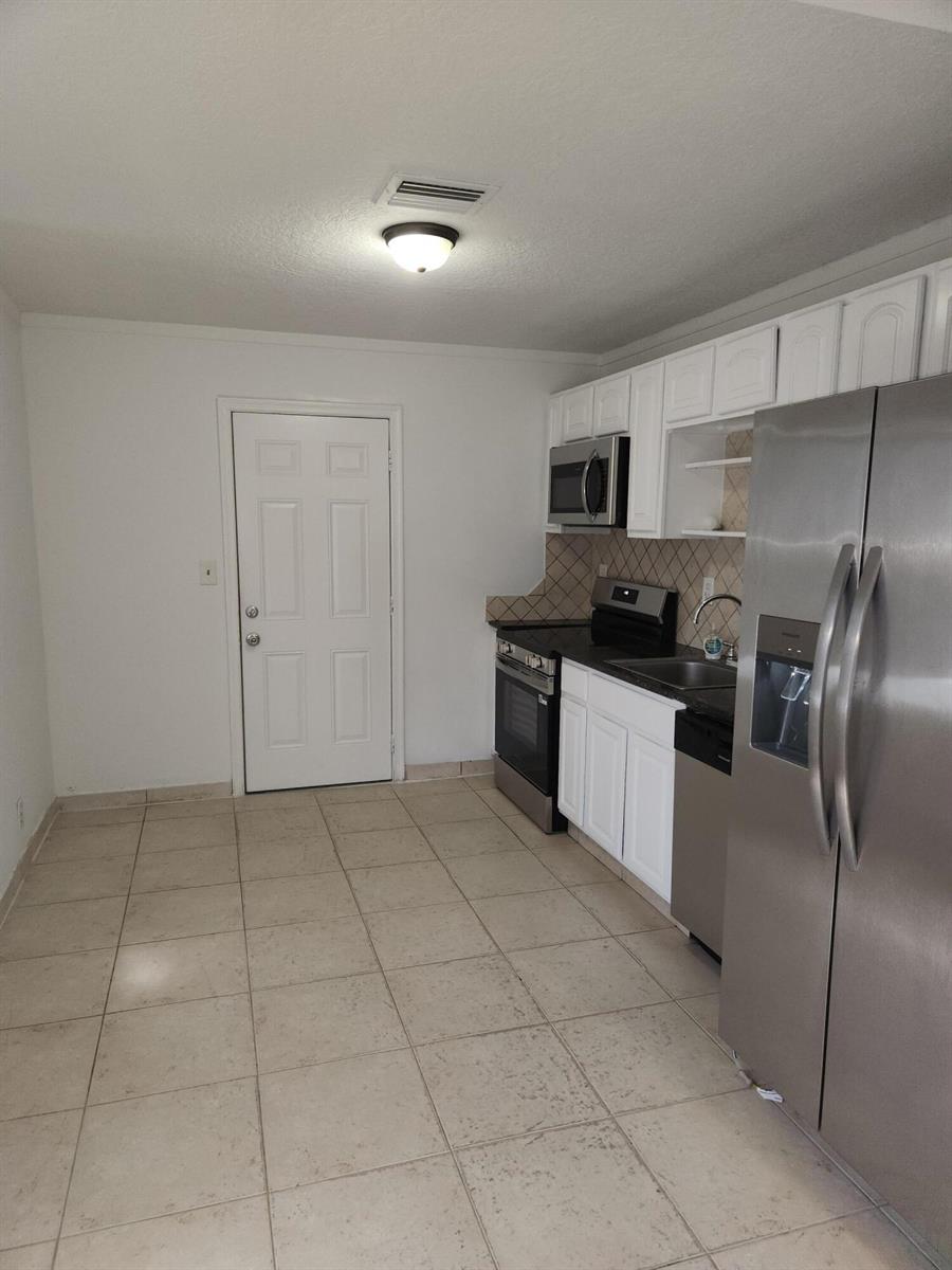 A kitchen features white cabinets, stainless steel appliances, a tiled backsplash, and light-colored floor tiles — 210 NW 13th Avenue, Delray Beach FL 33444, DELRAY BEACH, FL