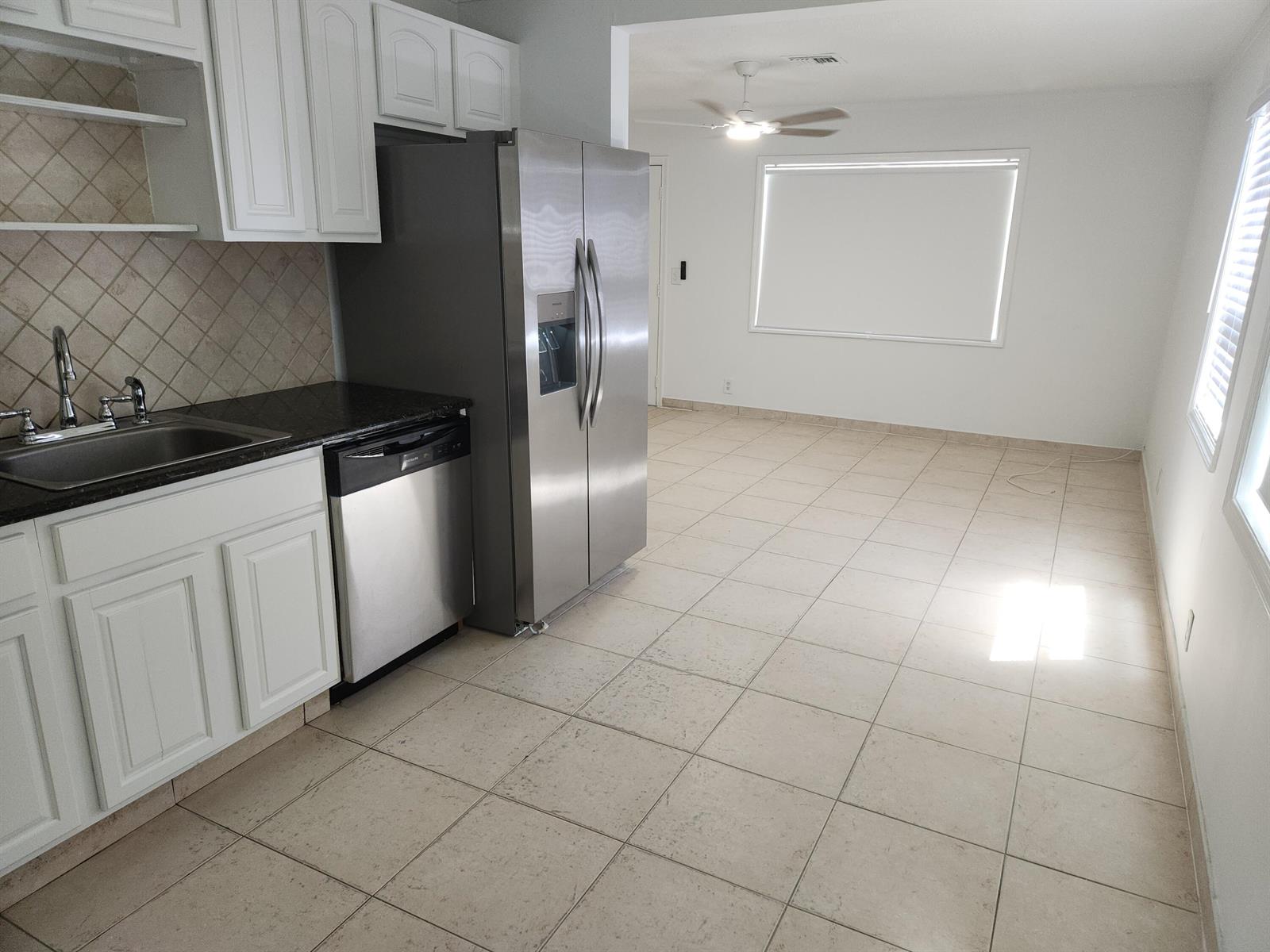 A kitchen with white cabinets, stainless steel appliances, and tile flooring opens to a dining area — 210 NW 13th Avenue, Delray Beach FL 33444, DELRAY BEACH, FL