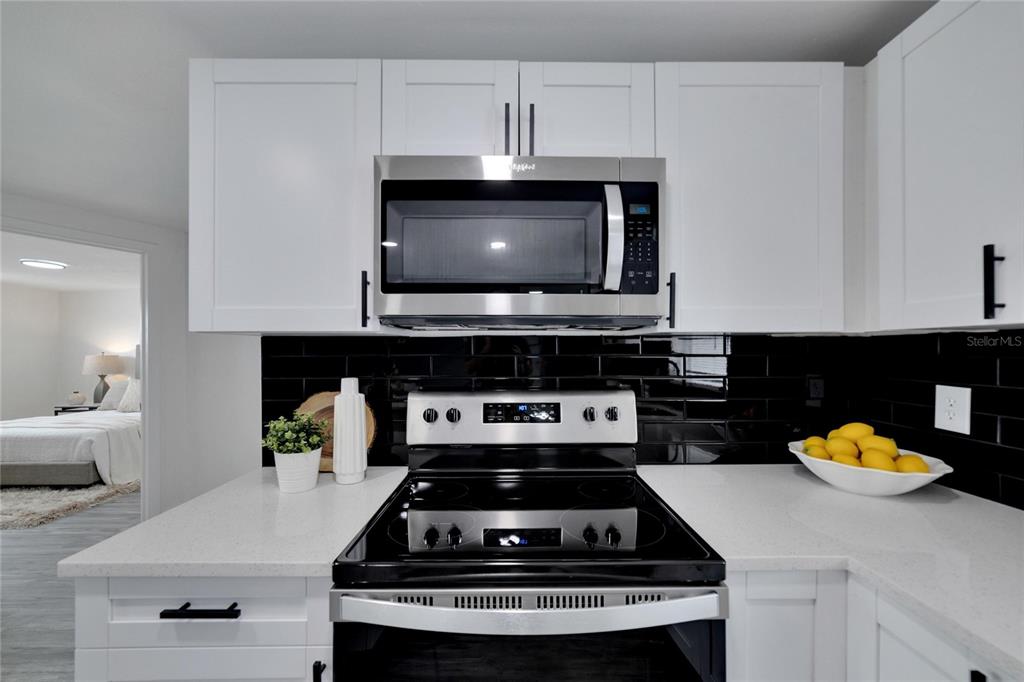 A kitchen features white cabinets, a stainless steel microwave, a black stove, and black backsplash — 4012 VALENCIA DRIVE, NEW PORT RICHEY, FL