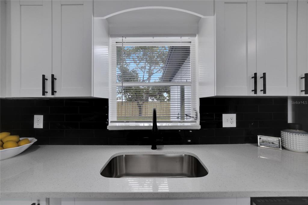 A kitchen sink sits below a window between white cabinets and a black tiled backsplash — 4012 VALENCIA DRIVE, NEW PORT RICHEY, FL