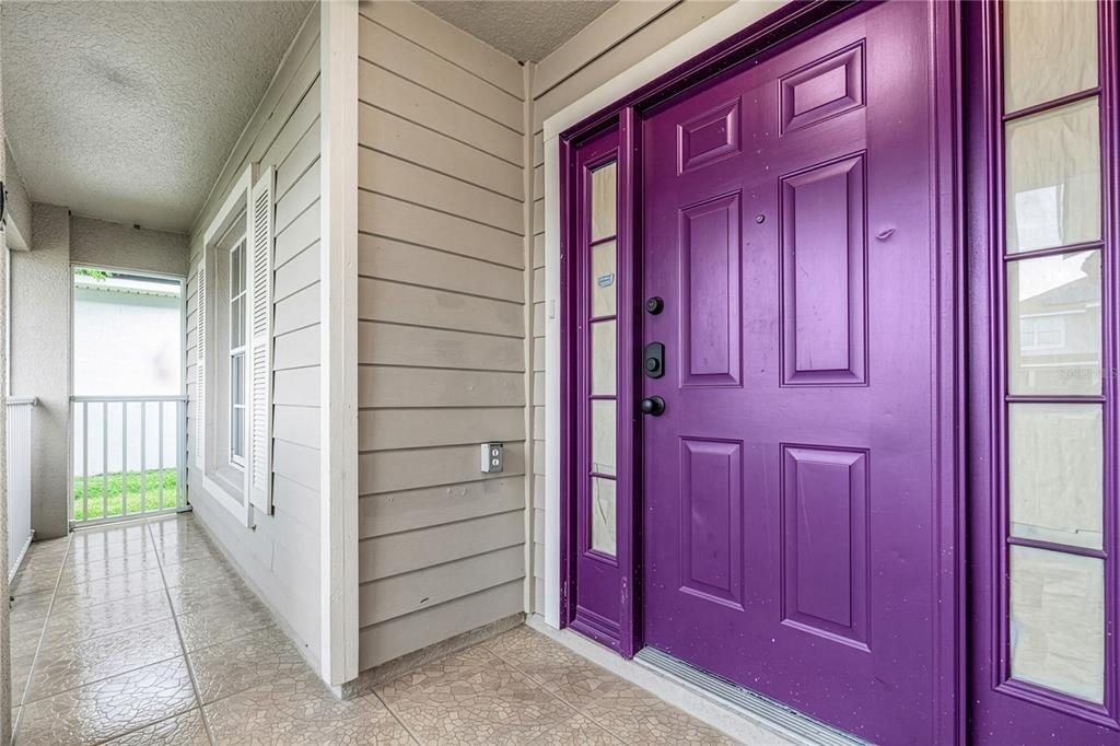 A purple front door with sidelights sits on a tiled porch next to beige siding — 2705 WILLOW GLEN CIRCLE, KISSIMMEE, FL