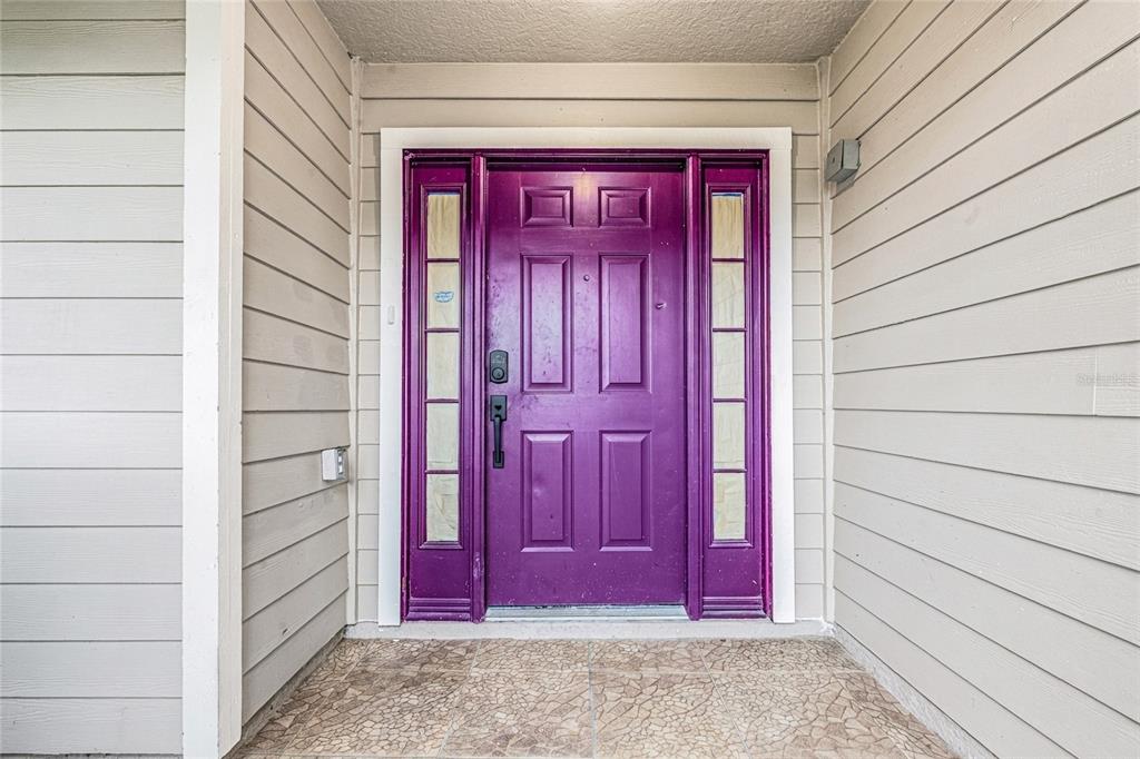 A purple front door with side windows is centered on a beige-sided house exterior — 2705 WILLOW GLEN CIRCLE, KISSIMMEE, FL