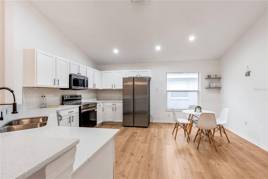 A kitchen with white cabinets, stainless steel appliances, and a small dining area — 2705 WILLOW GLEN CIRCLE, KISSIMMEE, FL