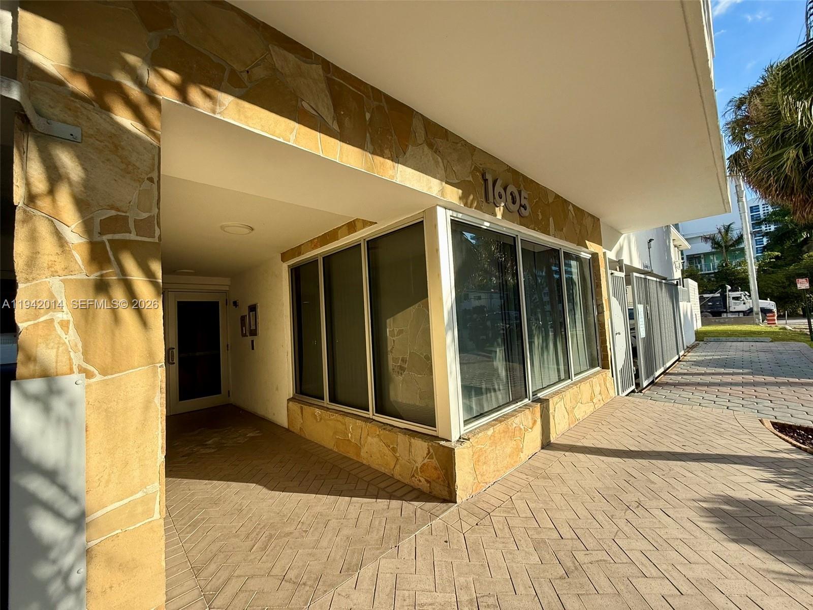The exterior of a building features stone cladding, a glass-enclosed corner, and a paved walkway — 1605 Bay Rd # 407, Miami Beach FL 33139, MIAMI BEACH, FL
