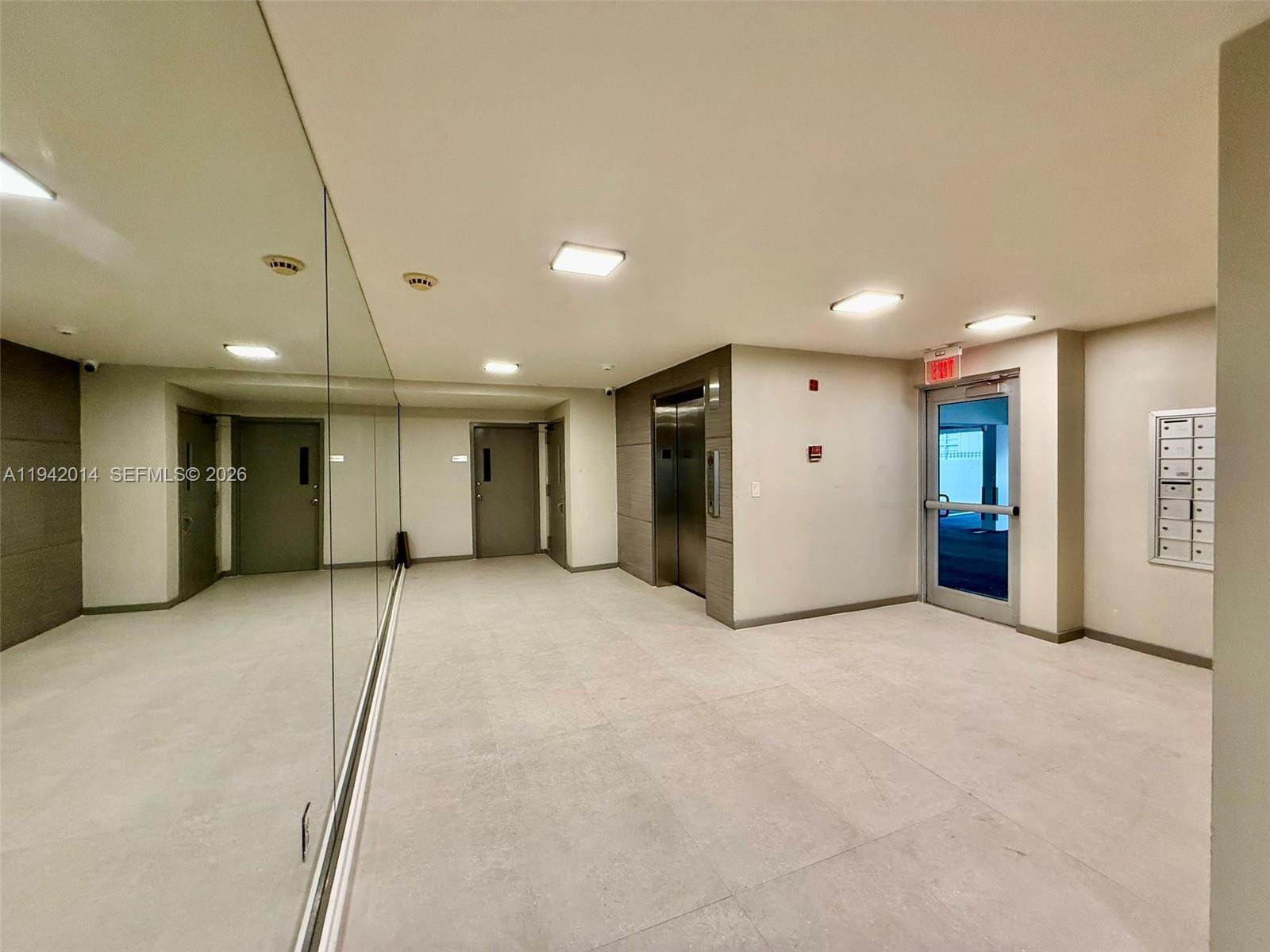 A hallway features light tile flooring, a mirrored wall, an elevator, and mailboxes — 1605 Bay Rd # 407, Miami Beach FL 33139, MIAMI BEACH, FL