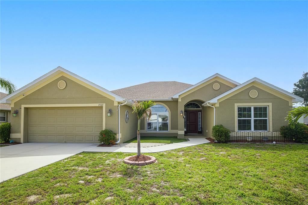 A single-story house with a tan stucco exterior, a two-car garage, and a palm tree — 1502 NAVIGATOR ROAD, PUNTA GORDA, FL