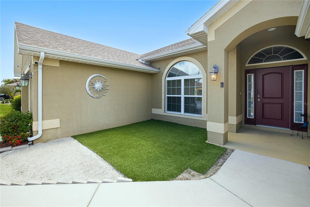 The exterior of a house features a tan stucco facade, a front door, and artificial turf — 1502 NAVIGATOR ROAD, PUNTA GORDA, FL