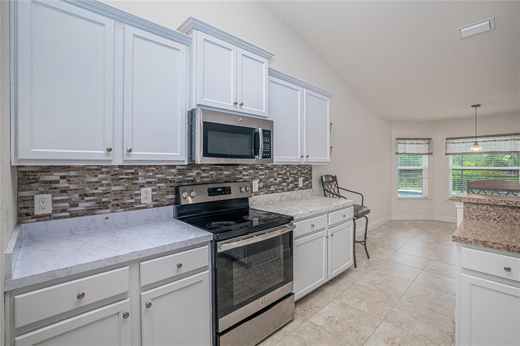 A kitchen features white cabinets, stainless steel appliances, a mosaic backsplash, and marble-look countertops — 1502 NAVIGATOR ROAD, PUNTA GORDA, FL