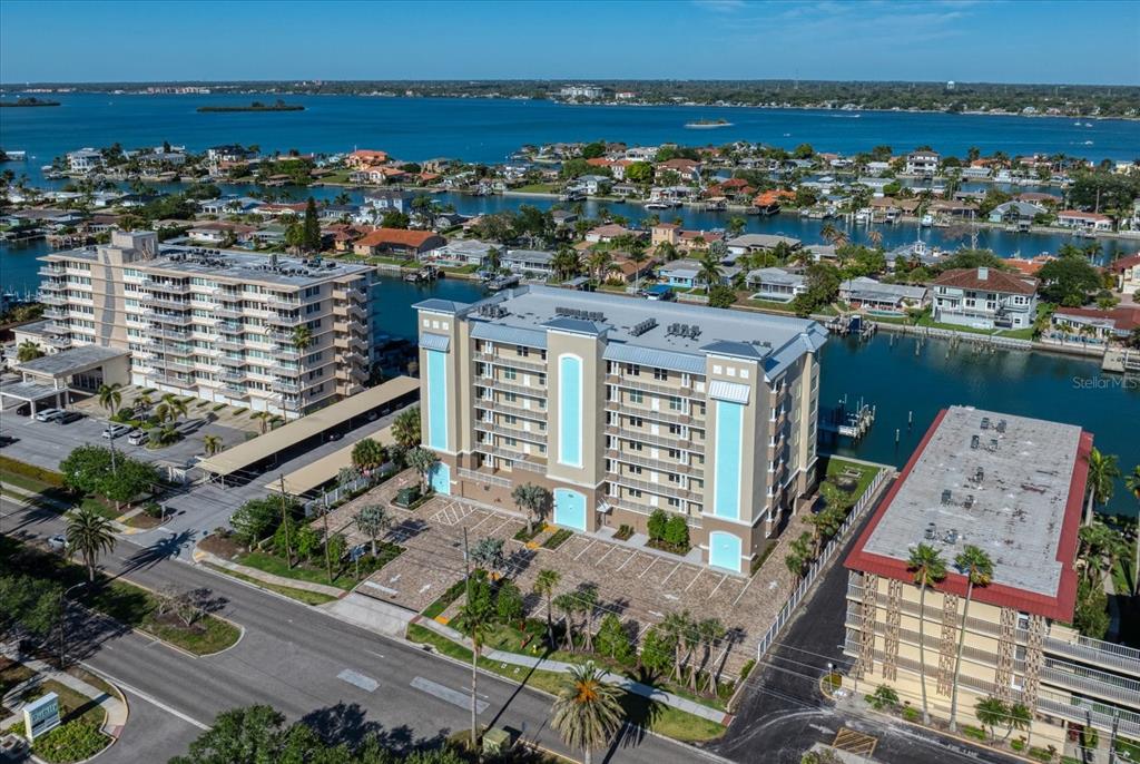 An aerial view shows a multi-story apartment building with a parking lot near water — 125 ISLAND WAY UNIT 402, CLEARWATER BEACH, FL