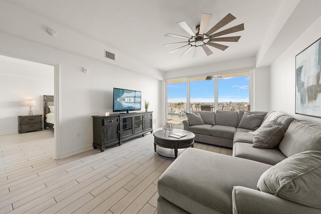 A living room with a grey sectional sofa, television console, and large windows overlooking water — 125 ISLAND WAY UNIT 402, CLEARWATER BEACH, FL