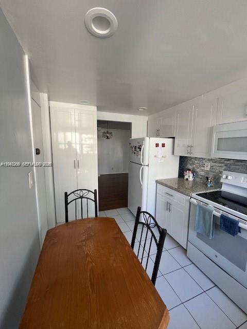 A kitchen with white cabinets, a wooden dining table, and a white refrigerator — MIAMI, FL