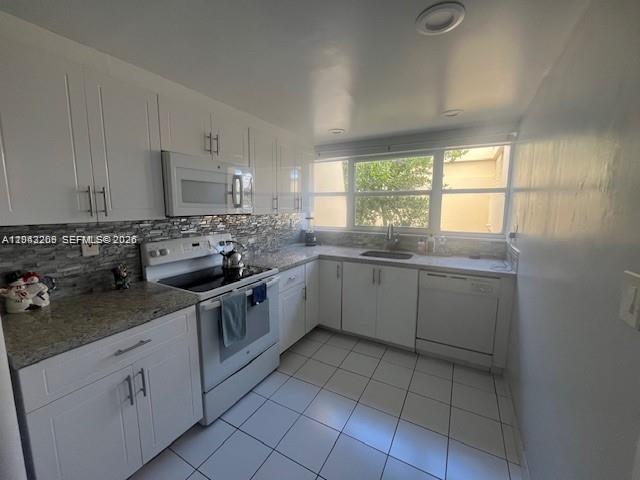 A kitchen features white cabinets, granite countertops, a tiled backsplash, and white appliances — MIAMI, FL