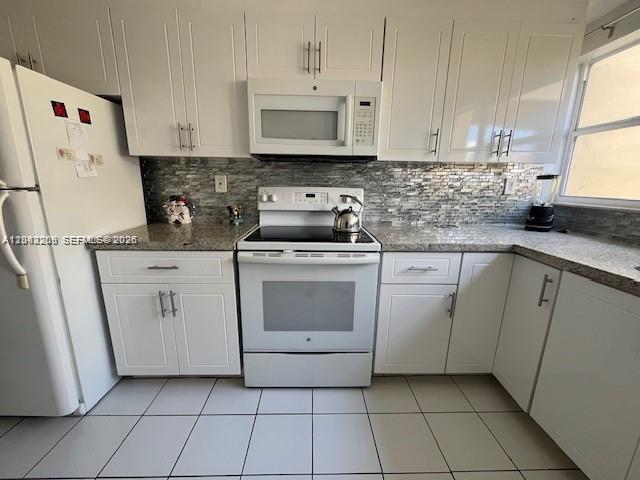 A kitchen features white cabinetry, a white stove, a microwave, and a tiled backsplash — MIAMI, FL