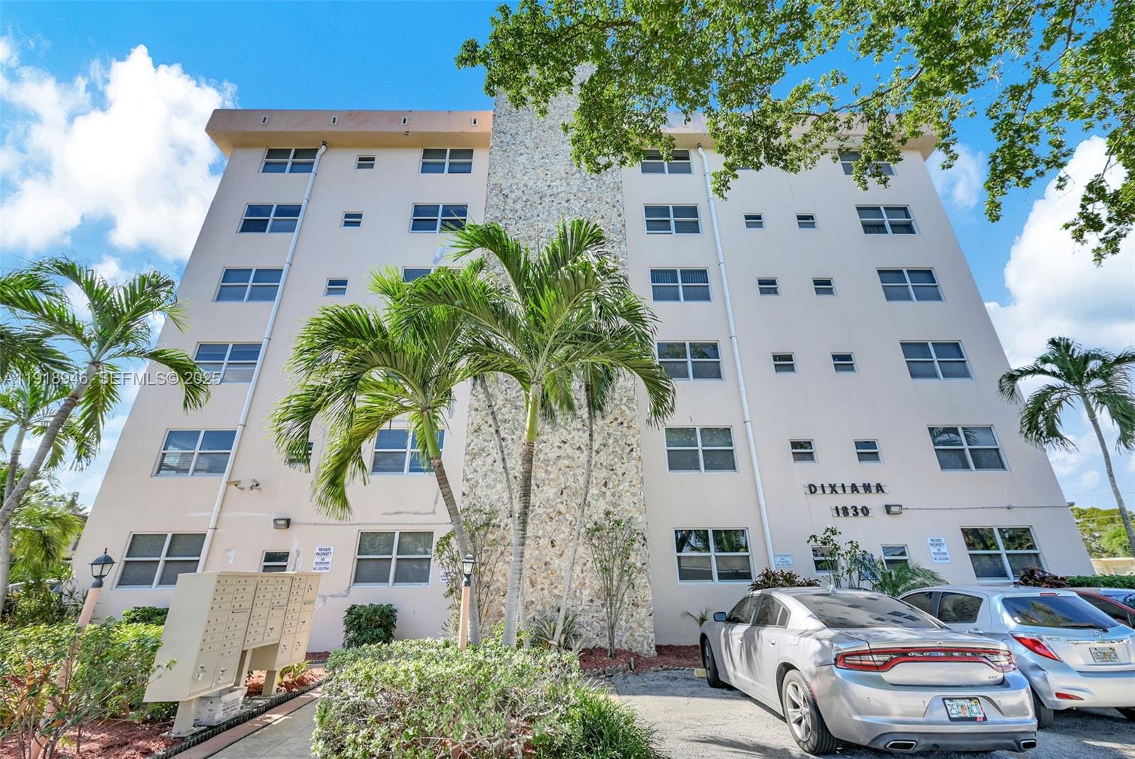 The exterior of a multi-story apartment building features a stone facade and palm trees — 1830 Dixieanna St # 506, Hollywood FL 33020, HOLLYWOOD, FL