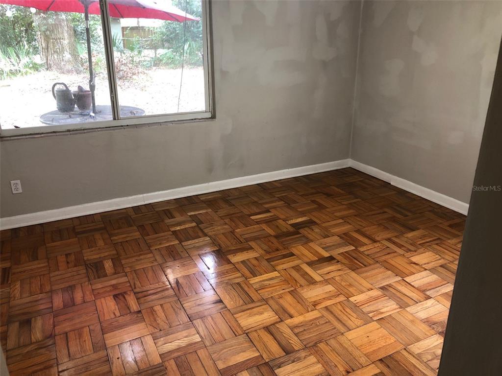 An empty room features parquet wood flooring, light gray walls, and a large window — 304 NW 36TH STREET, GAINESVILLE, FL