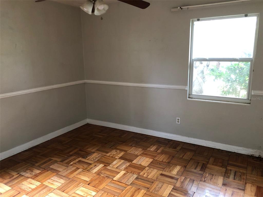 An empty room features parquet wood flooring, light gray walls with chair rail molding, and a window — 304 NW 36TH STREET, GAINESVILLE, FL