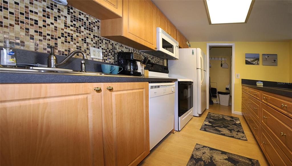 A kitchen features light wood cabinets, a mosaic tile backsplash, and white appliances — 1571 S ATLANTIC AVENUE UNIT 312, NEW SMYRNA BEACH, FL